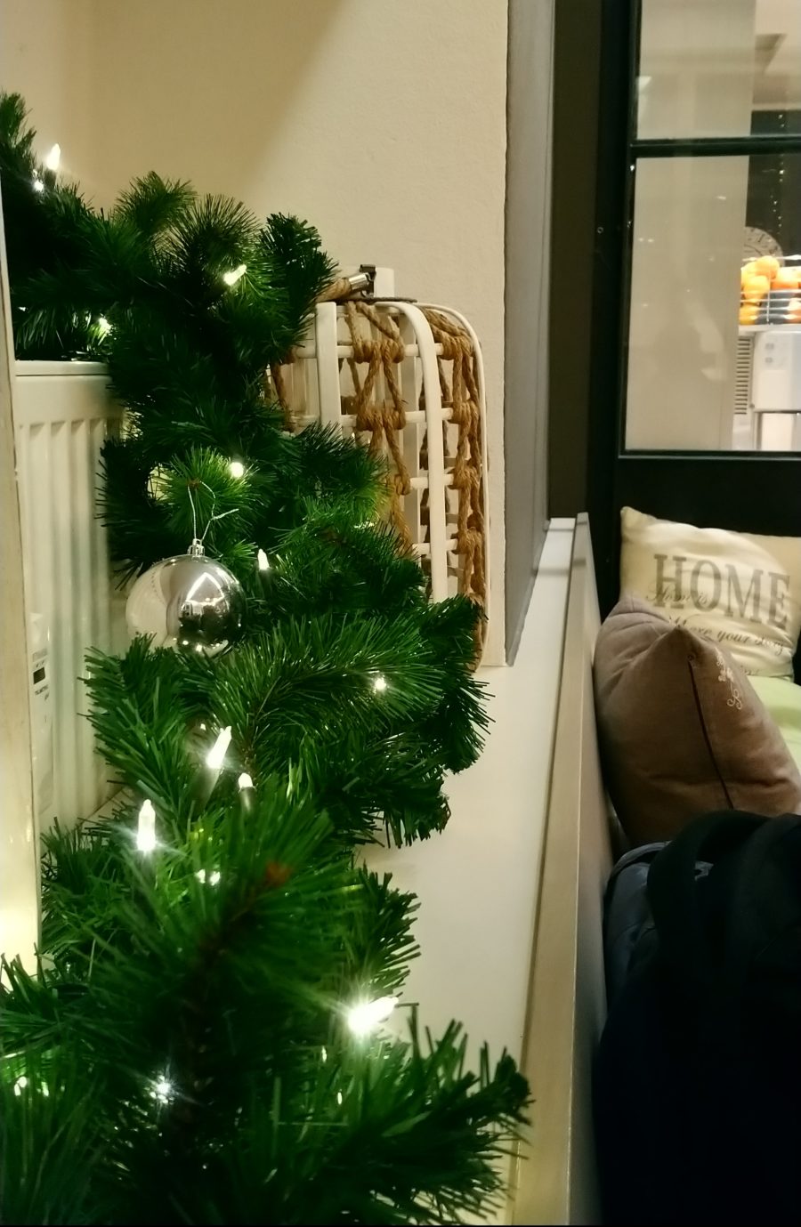 Weihnachtsgirlande mit Lichterkette und silberner Kugel auf der Fensterbank
