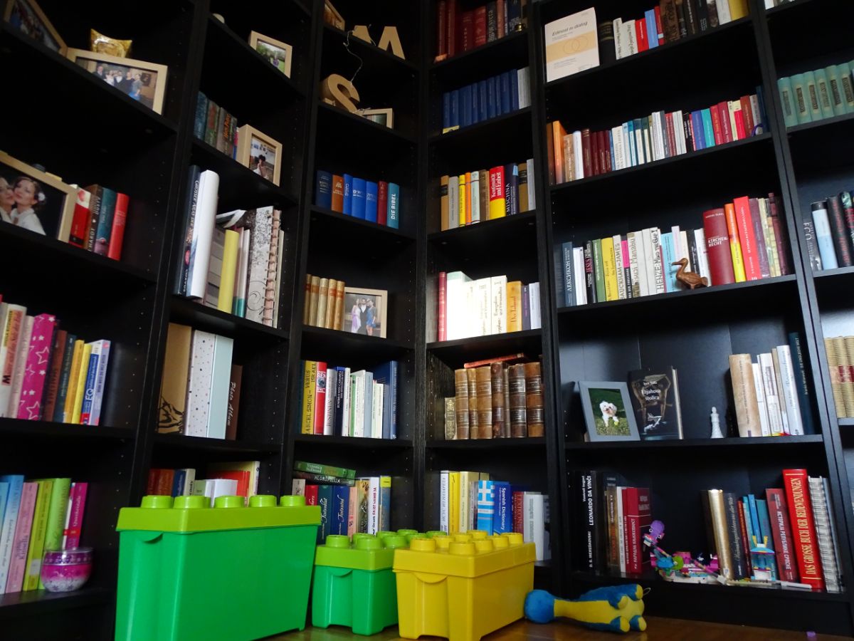 Bibliothek zu Hause voller Bücher, davor Lego-Duplo-Spielzeugkisten auf dem Boden