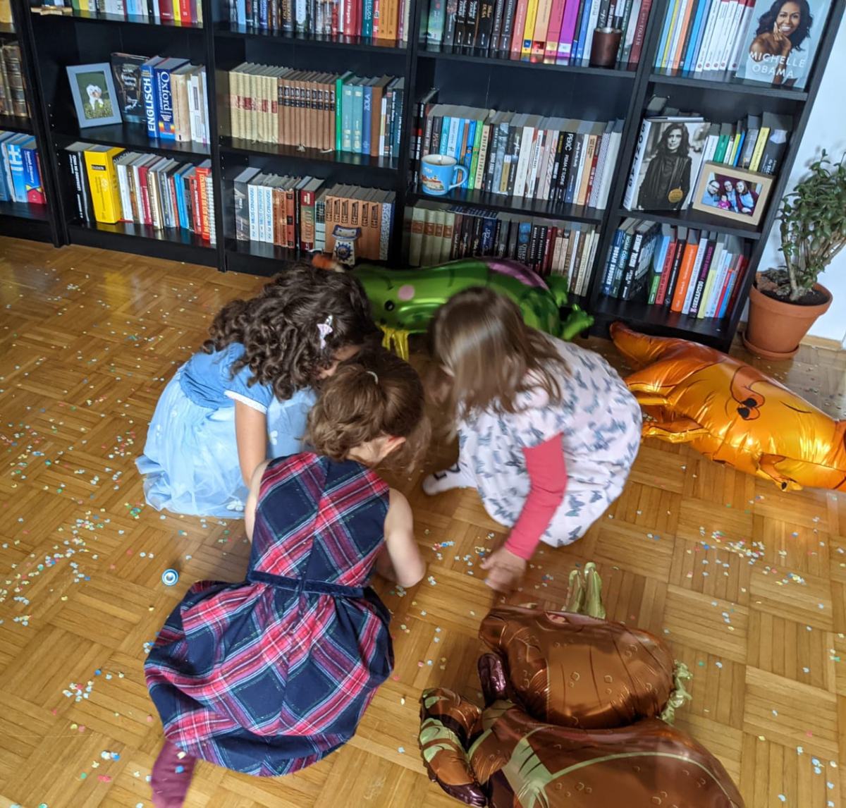 Tri devojčice se igraju na podu ispred police sa knjigama