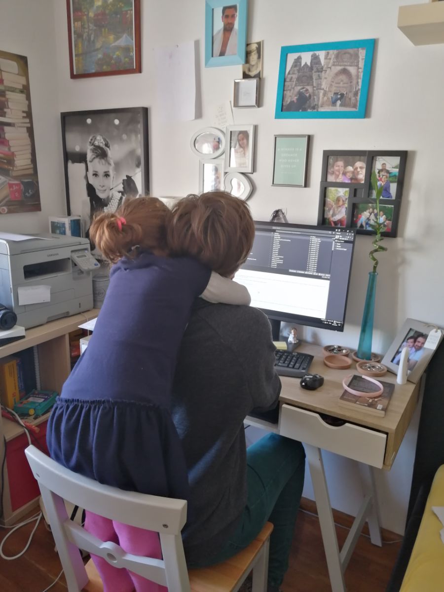 Devojčica grli mamu dok radi za kompjuterom kod kuće