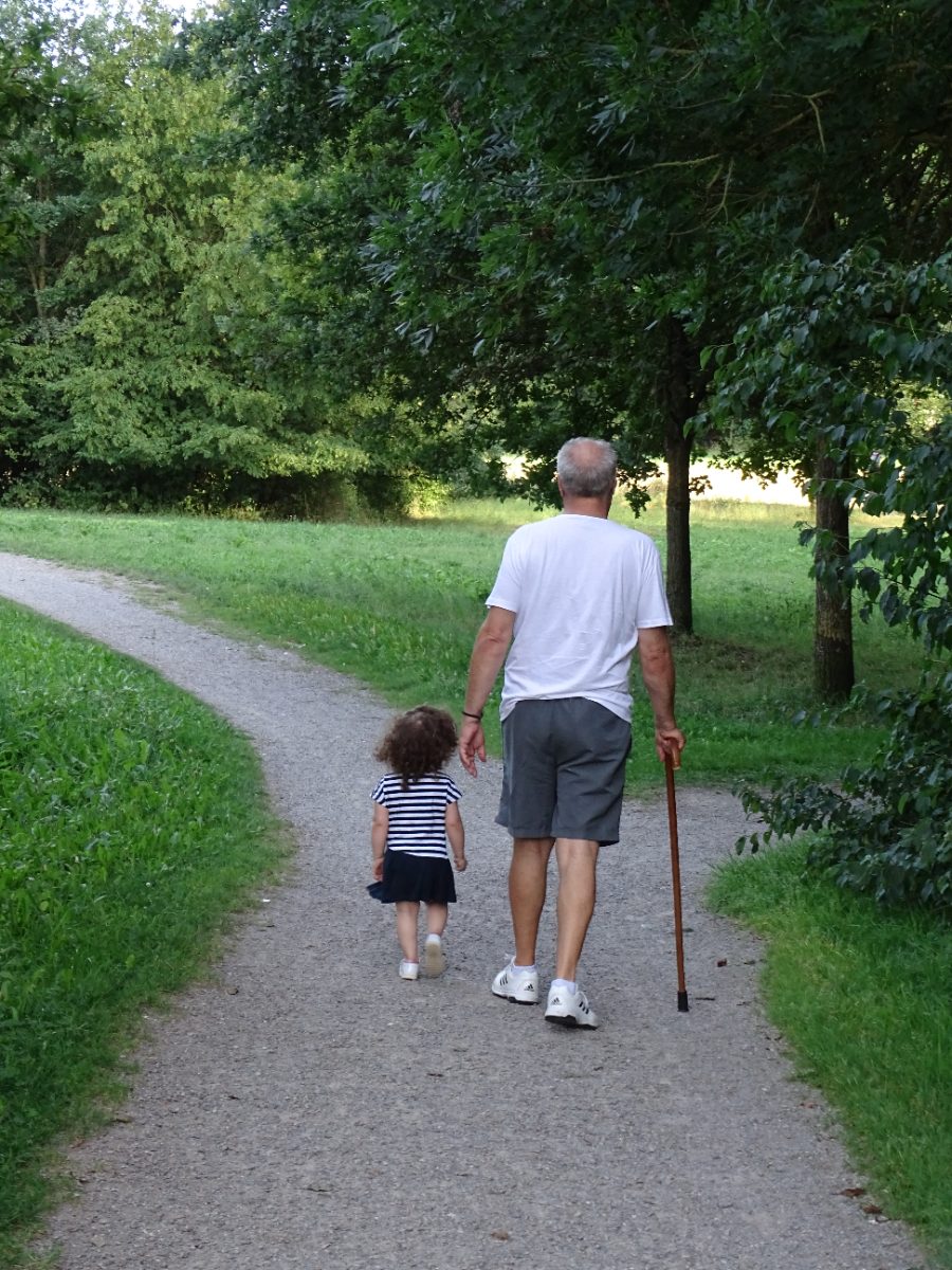 Sofia and her grandpa walking down a park path, seen from behind