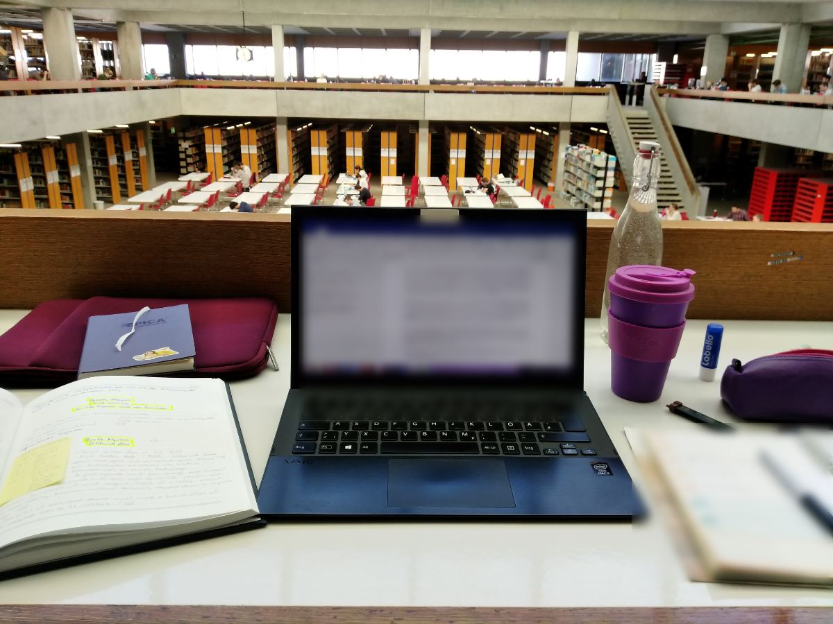A laptop, notes and a coffee cup on a desk in the university reading room
