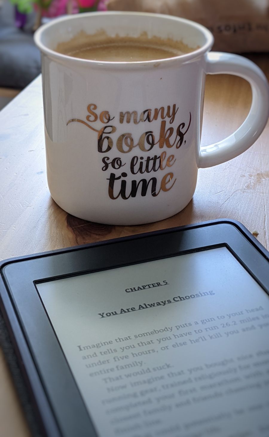 Eine Kaffeetasse mit der Aufschrift „So many books, so little time“, davor ein Kindle
