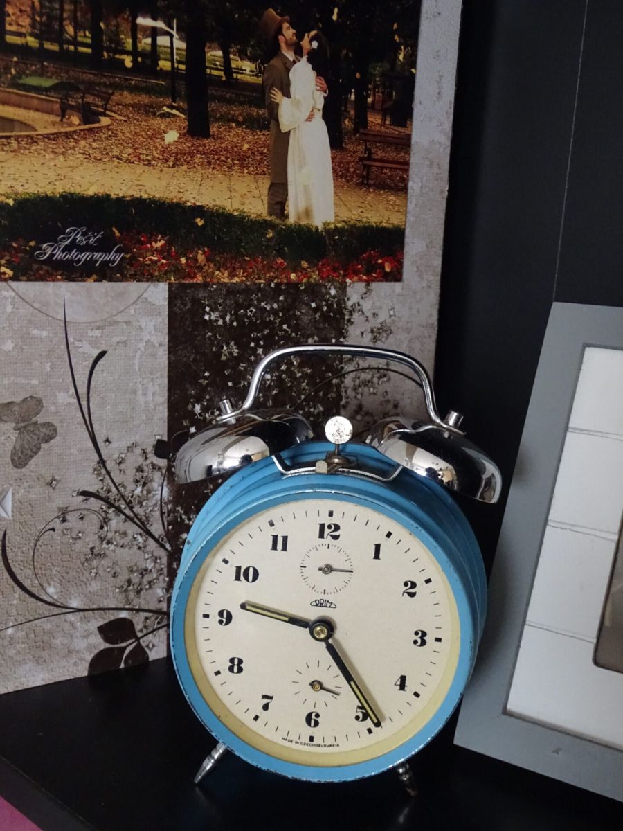 Old blue alarm clock on a shelf with a wedding photo in the background